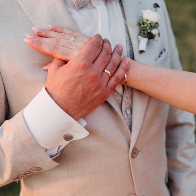 Hände eines Hochzeitspaares auf dem Anzug des Bräutigams im Abendlicht auf dem Einkorn in Schwäbisch Hall.