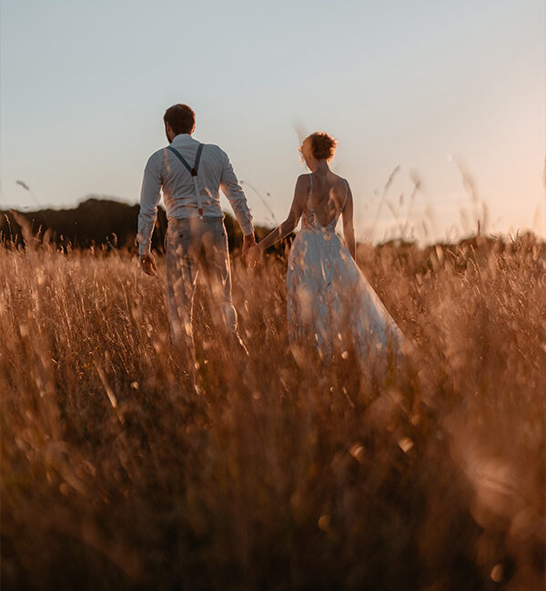 Hochzeitspaar läuft bei Sonnenuntergang durch ein Feld in Engelhardshausen bei Blaufelden.